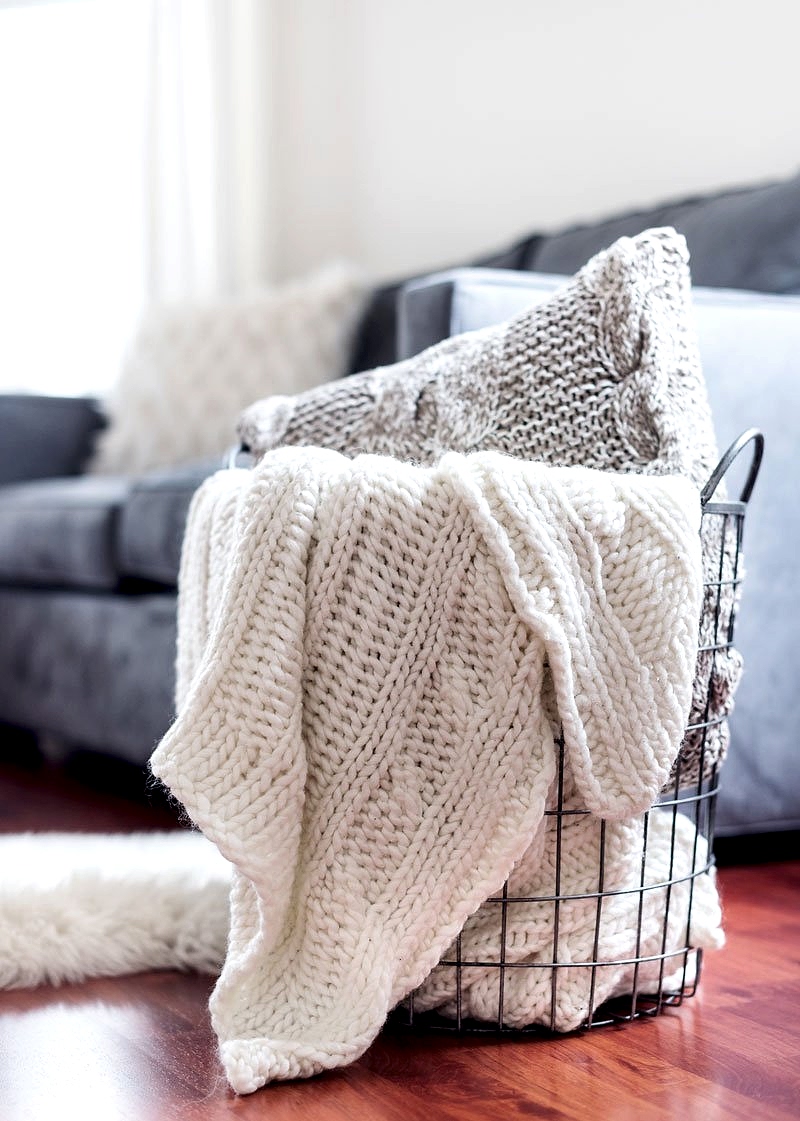 A basket full of blankets and pillows in a living room.
