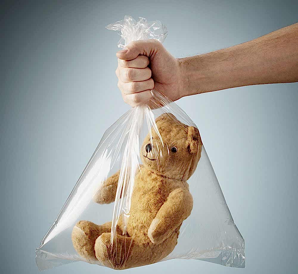 A hand holding a teddy bear in a plastic bag.