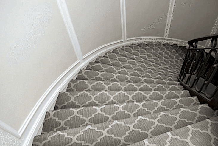a curved staircase with patterned gray carpet and a dark railing, viewed from the top looking down.