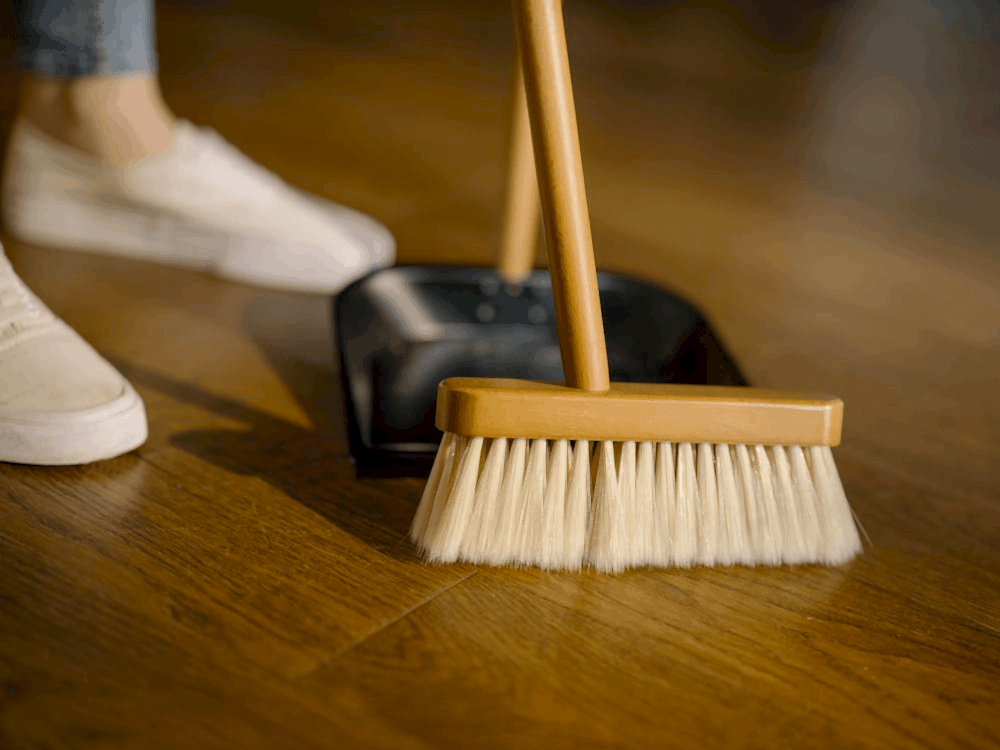 close-up of a brow wooden broom being used to clean a wooden floor