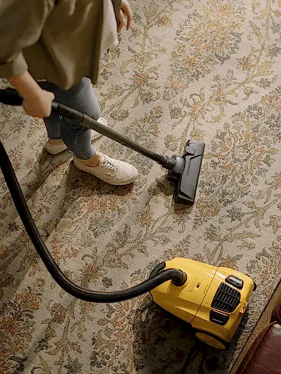 a person using a yellow vacuum cleaner on a rug